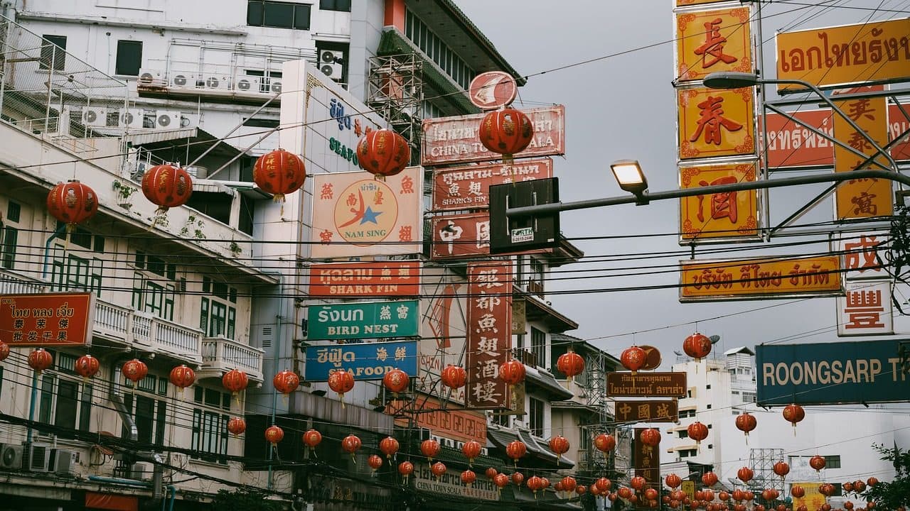 Shop signs and red lanterns strung across a street in Bangkok's Chinatown