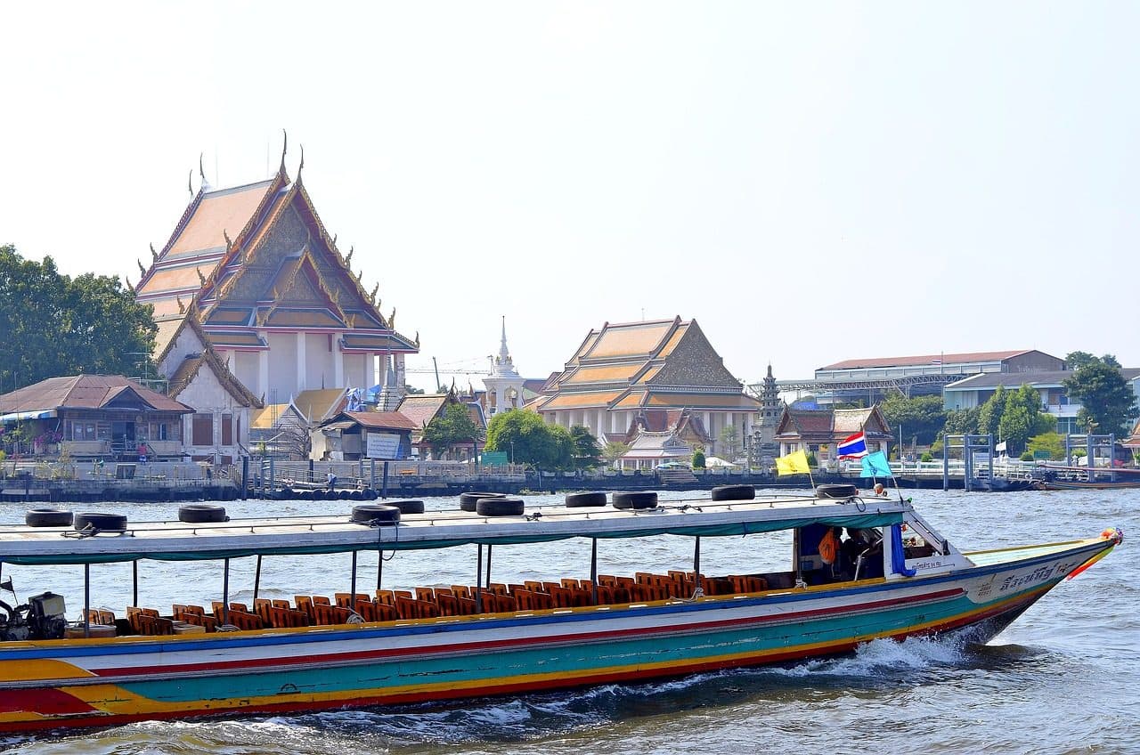 A long-tail boat on the river in front of riverside temple buildings