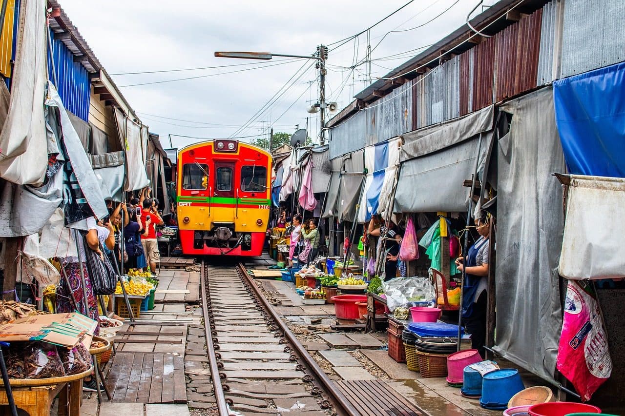 A yellow train approaching through the stalls of the Maeklong Railway Market