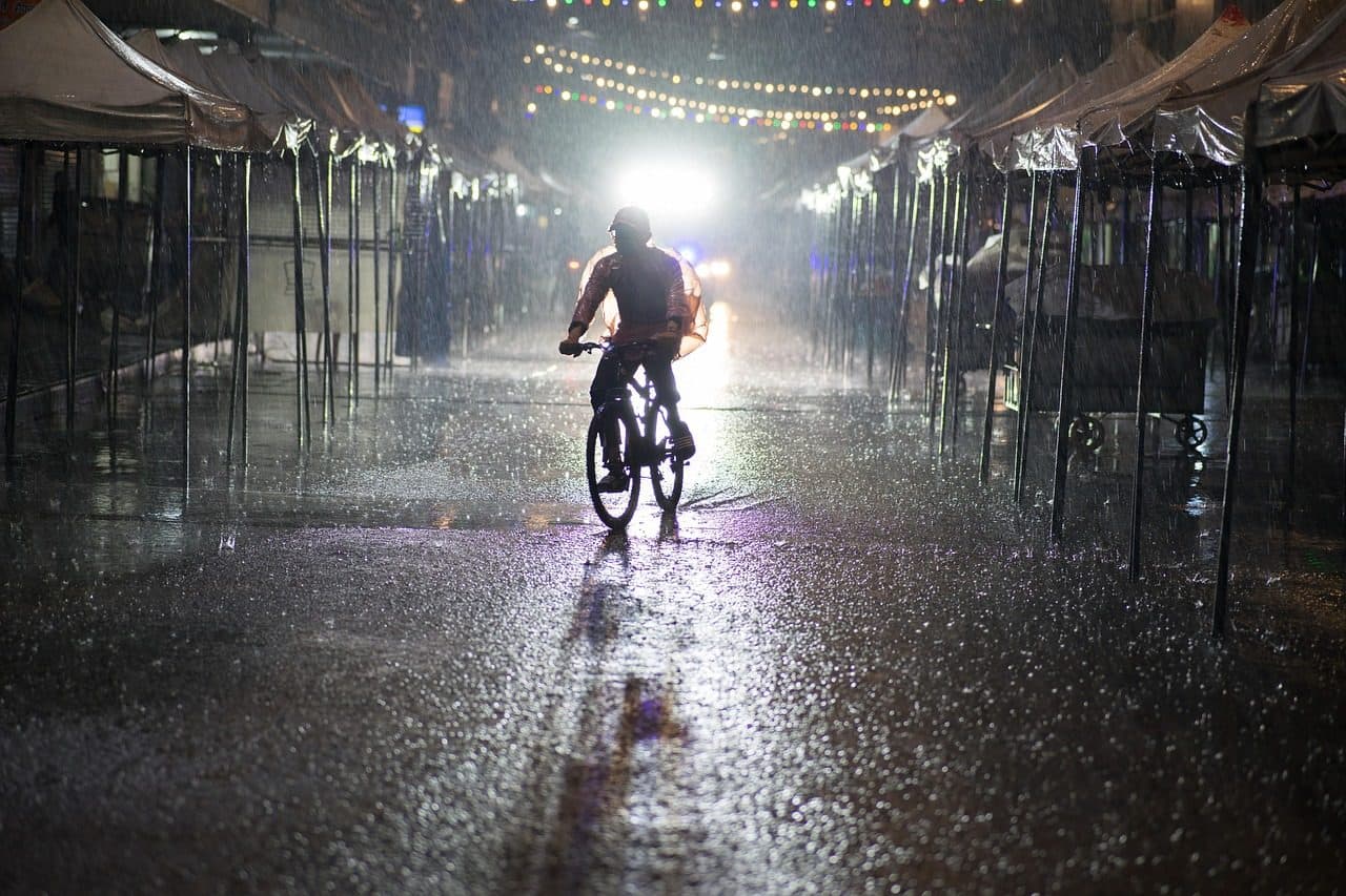A cyclist riding through a rain-soaked night market lane