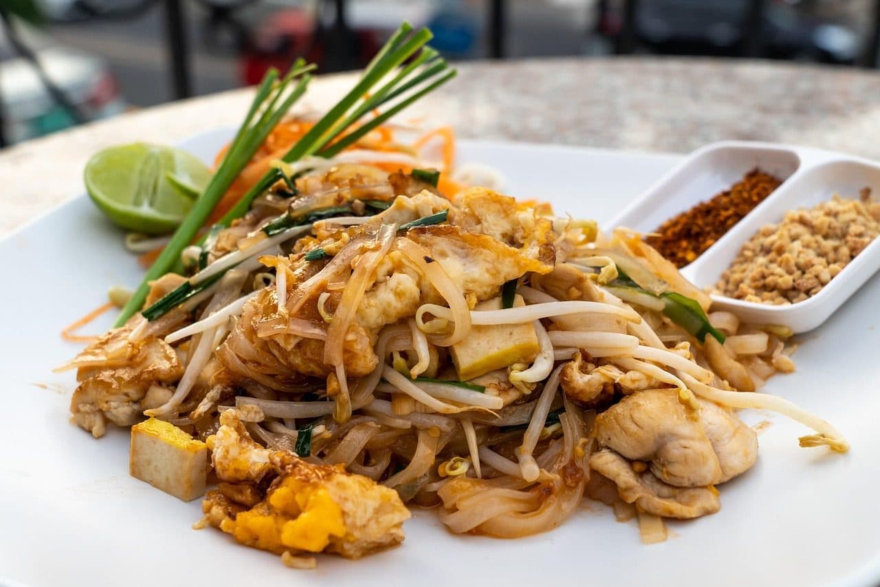 A plate of pad thai with lime, bean sprouts and chilli flakes on the side
