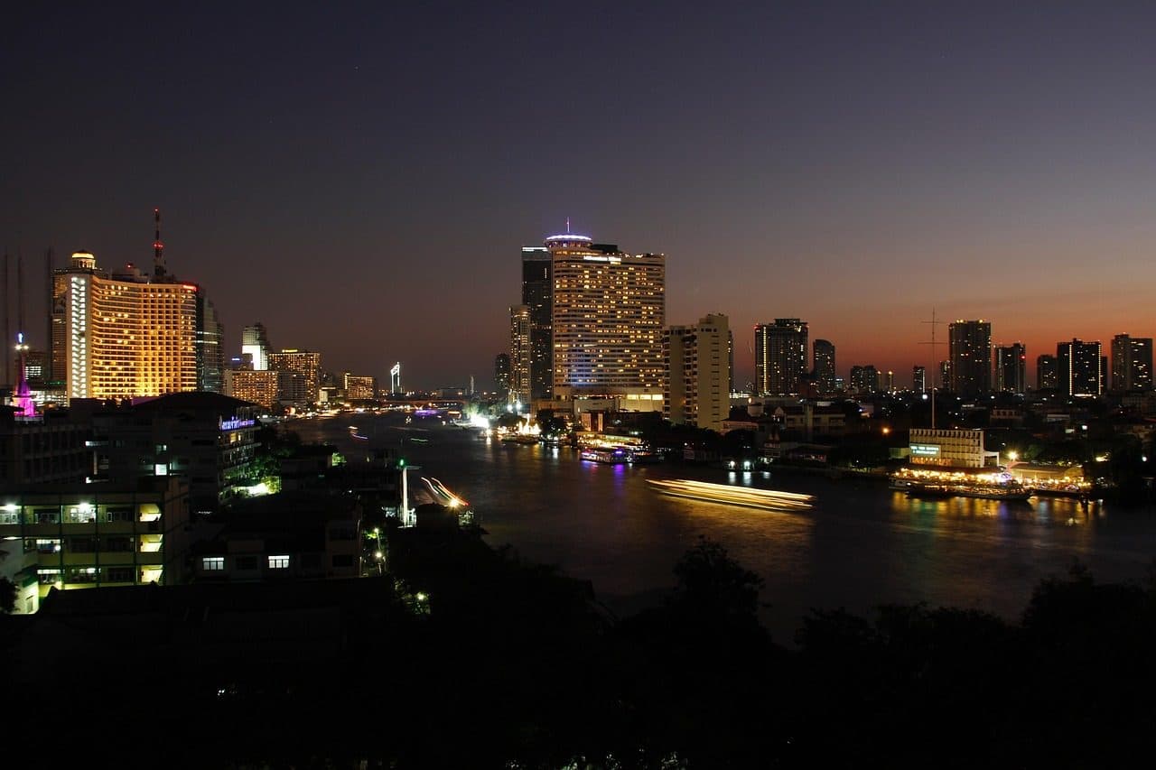 Riverside towers and hotels lit up at dusk along the Chao Phraya